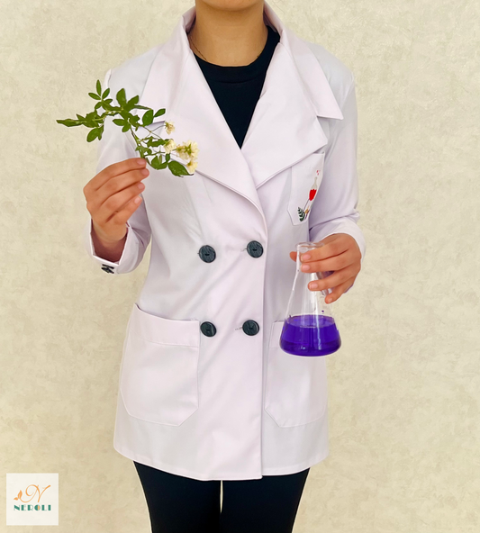 A laboratory professional wearing a white peak lapel coat and standing with a small leaf in their right hand and a flask in their left hand