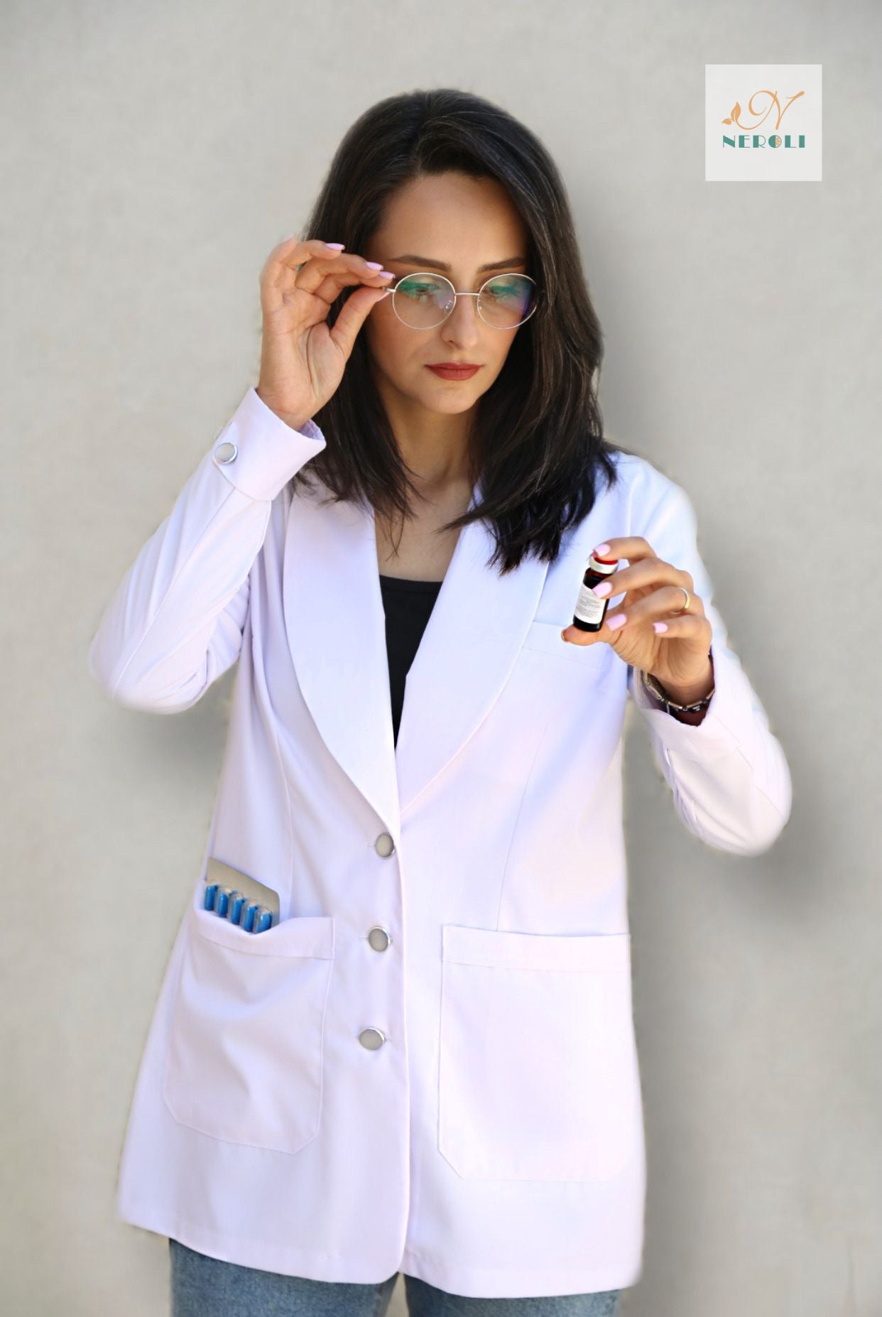 Medical nurse in white coat examining injection liquid bottle with left hand, touching eyeglasses with right hand.