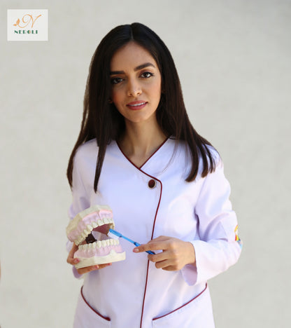 A close-up of female dentist in lab coat with dark red piping, holding a toothbrush and duplicate teeth set.