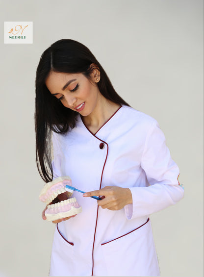 A female dentist wearing a full sleeve coat, standing with a set of teeth and a toothbrush.